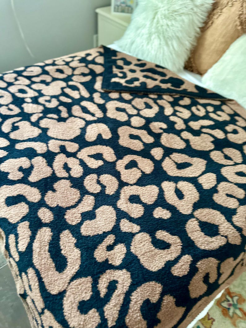 May include: A plush throw blanket with a black and brown leopard print pattern. The blanket is soft and fuzzy, perfect for cuddling up on the couch.