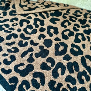 May include: A soft, plush throw blanket with a leopard print pattern in black and tan colors. The blanket is folded and displayed on a bed.