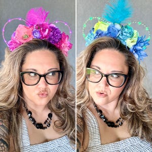 May include: Two women wearing floral headbands with light-up ears. The headband on the left is pink, purple, and green. The headband on the right is blue, green, and yellow.