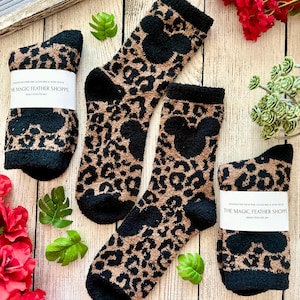 May include: Pair of black and brown fuzzy socks with a leopard print and a Mickey Mouse silhouette. The socks have a tag that reads "The Magic Feather Shoppe".
