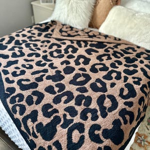 May include: A plush throw blanket with a black and brown leopard print design. The blanket is made of a soft, fuzzy material and is perfect for adding a touch of style and warmth to any room.