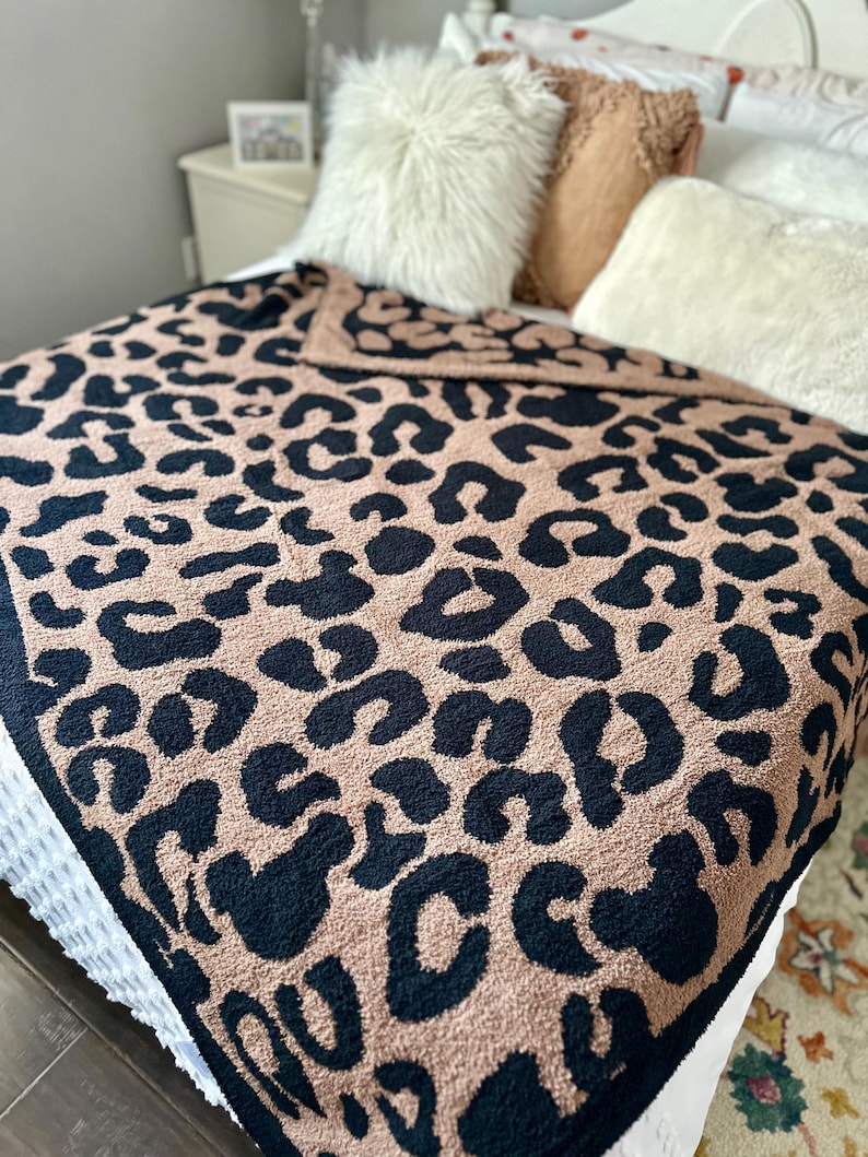 May include: A plush throw blanket with a black and brown leopard print design. The blanket is made of a soft, fuzzy material and is perfect for adding a touch of style and warmth to any room.
