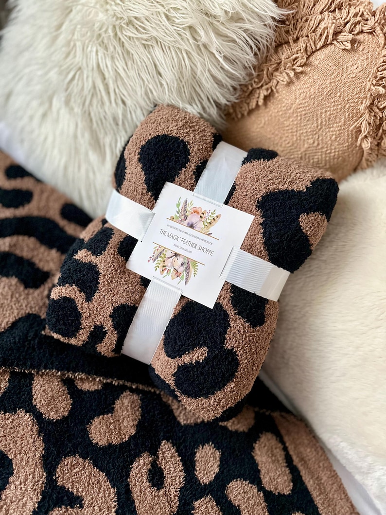 May include: A brown and black leopard print throw blanket with a white ribbon tied around it. The ribbon has a tag that says "The Magic Feather Shoppe".