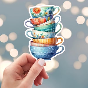 May include: A stack of six colorful teacups with floral and geometric patterns. The cups are stacked in a whimsical way, with the top cup tilted slightly. The cups are painted in shades of blue, green, orange, and yellow.