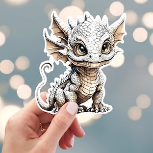 May include: A white and brown cartoon dragon sticker with a curled tail and large eyes. The dragon is smiling and has a textured, scaly body.