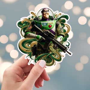 Pu&ograve; includere: Un adesivo verde e oro con un personaggio dei cartoni animati che tiene un fucile. Il personaggio indossa un'uniforme mimetica verde e marrone e un casco. Il personaggio &egrave; circondato da vortici verdi e dorati.