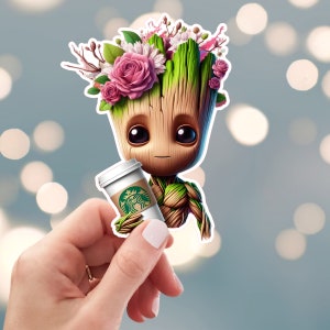 May include: A green cartoon character with a flower crown holding a green and white coffee cup. The character has a brown face and large eyes.
