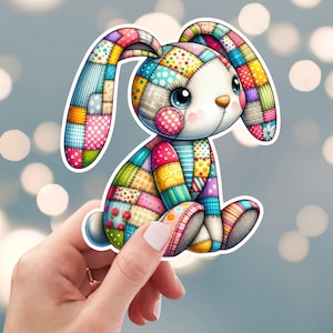 May include: A colorful patchwork bunny with a white face and blue eyes. The bunny is sitting with its legs crossed and its ears are perked up.