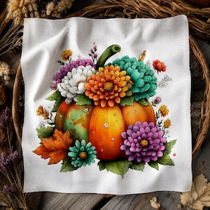 May include: A white fabric square featuring a central illustration of an orange pumpkin adorned with a vibrant bouquet of colorful flowers including purple, white, orange, and teal chrysanthemums, green leaves, and a single orange maple leaf.
