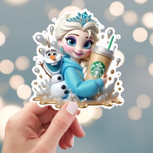 May include: A sticker featuring a cartoon illustration of Elsa from Frozen holding a Starbucks coffee cup.  Elsa is wearing a blue hoodie and a crown.  Olaf is standing behind her.  The sticker is surrounded by a gold liquid splash.