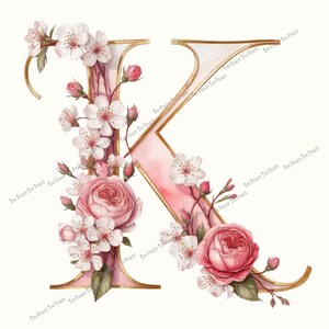 May include: A floral letter "K" design. The letter is outlined in gold with a pink watercolor fill. Pink roses, buds, and white blossoms adorn the letter. The words "Tee Peace Tee Peace" are printed on the letter.