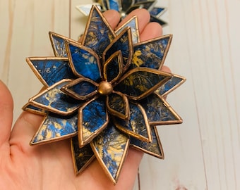 Puede incluir: Una flor de vidrio tintado azul y dorado con detalles en cobre. La flor tiene forma de estrella y está hecha de varias capas de vidrio.