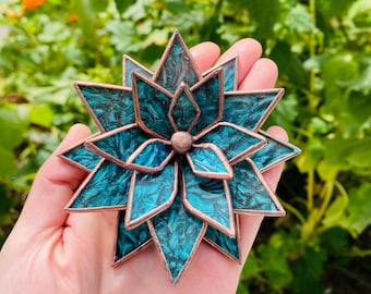 Puede incluir: Una flor de vidrio teñido de color azul turquesa con detalles en cobre. La flor tiene forma de estrella con múltiples capas de pétalos.