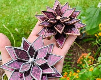 Puede incluir: Dos adornos de flores de suculentas de vidrio tintado. El adorno más grande es de color rosa intenso con un contorno plateado. El adorno más pequeño es de color rosa más oscuro con un contorno de cobre.