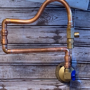 May include: Copper pipe plumbing fixture with two valves and a brass base. The pipe is bent into a curved shape and has a horizontal section.