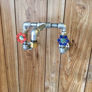 May include: Two silver metal spigots with red and blue handles mounted on a wooden wall. The spigots are connected by a silver metal pipe.