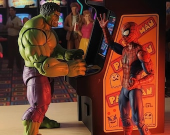 May include: Action figures of the Hulk and Spider-Man playing a Pac-Man arcade game. The arcade cabinet has the Pac-Man logo and character graphics. The background shows other arcade games and neon signs.