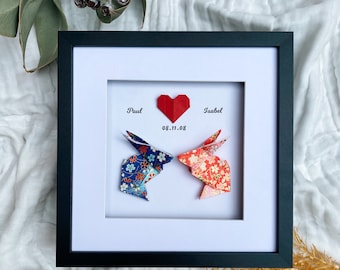 May include: Framed origami art featuring two paper rabbits facing each other, with a red heart above them. The rabbits are made of patterned paper in blue and red. The names "Paul" and "Isabel" and the date "08.11.08" are printed above the rabbits.