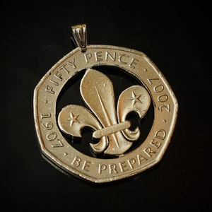 May include: A gold-colored pendant made from a 50 pence coin with a cut-out of the Scout's fleur-de-lis symbol. The coin reads "Fifty Pence 1967-2007" and "Be Prepared".