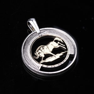May include: Silver pendant with a gold-colored antelope design. The pendant is round and has a textured edge.