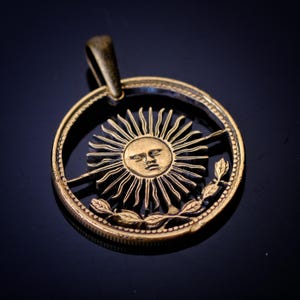 Pingente de moeda de 1 peso com corte de sol argentino. Lapidado à mão.