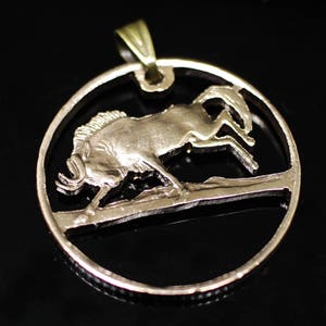 Pode incluir: Um pingente de moeda de prata com um recorte detalhado de um gnu correndo. A moeda está presa a um anel de salto de latão.