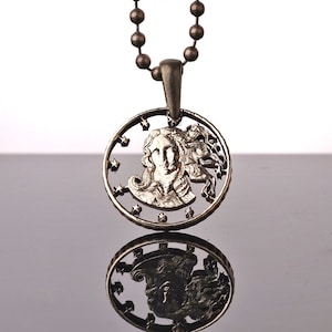 Puede incluir: Un collar de plata con un colgante que presenta un recorte de la cara de una mujer con estrellas alrededor del borde.