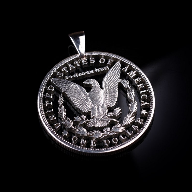 Pu&ograve; includere: Una moneta d'argento da un dollaro con l'aquila tagliata, lasciando solo il contorno dell'aquila. La moneta &egrave; un ciondolo con un anello in cima per appenderla. La moneta recita "United States of America, In God We Trust, One Dollar".
