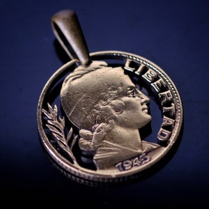 May include: A gold-colored coin pendant with a profile of a woman's face and the word "LIBERTAD" inscribed around the edge. The year "1945" is also visible on the coin.