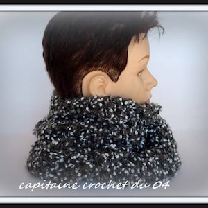 Peut inclure: Une écharpe infinie en crochet gris et blanc. L'écharpe est portée par un mannequin aux cheveux courts bruns.