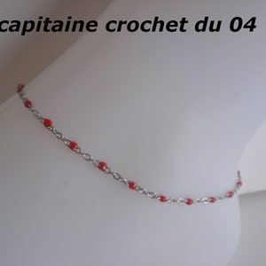 Peut inclure: Un bracelet de cheville en chaîne argentée avec des perles rouges. Le bracelet est sur un fond blanc.