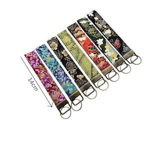 May include: A collection of seven fabric key fobs, each featuring a unique floral pattern in various colors. The fobs are approximately 5.5 inches long and have a metal ring for attaching keys. The patterns include cherry blossoms and other Japanese-inspired designs.