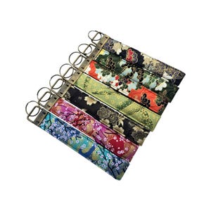 May include: A collection of key fobs with floral patterns in various colors, including blue, pink, red, green, and gold. Each fob has a metal ring and a fabric strap with a Japanese-inspired design.