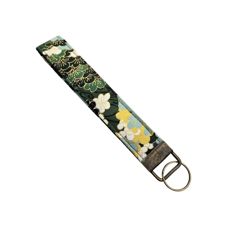 May include: A fabric wristlet key fob with a floral pattern in shades of green, yellow, and blue. The key fob has a bronze-colored metal clasp and key ring. The fabric is approximately 1 inch wide.