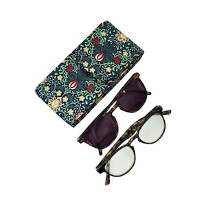 May include: A rectangular glasses case featuring a dark green fabric with a dense floral and leaf pattern in red, yellow, and light green. Beside the case are two pairs of glasses with brown tortoiseshell frames, one with dark lenses and one with clear lenses.