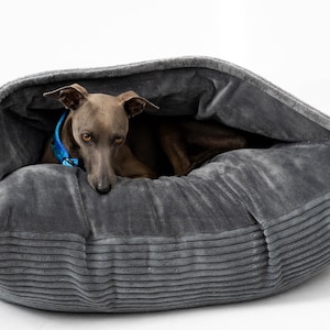 May include: A gray dog bed with a hooded design, featuring a gray dog wearing a blue collar. The bed has a corduroy texture and is designed for comfort. The dog is a light gray color.