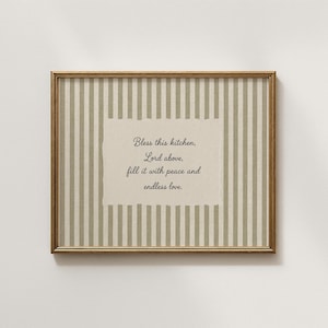 Pode incluir: Uma impressão de arte de parede retangular numa moldura dourada fina com um fundo de riscas verticais bege e branco. Centrado está um inserto de papel creme com o texto: Bless this kitchen, Lord above, fill it with peace and endless love.