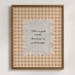 May include: A framed wall art print featuring a light brown and white gingham pattern background. Centered is a textured off-white paper square with a white lace border, displaying the black text: Fall is a gentle reminder that change can be beautiful.