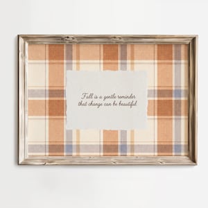 May include: A rectangular wall art piece in a weathered wood frame featuring a plaid pattern in shades of orange, cream, and blue. Centered is a white paper cutout with torn edges displaying the text: Fall is a gentle reminder that change can be beautiful.