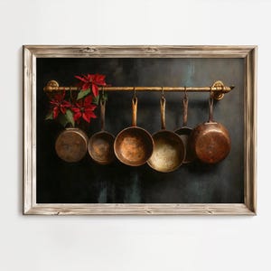 Puede incluir: Impresión enmarcada que muestra una colección de sartenes de cobre colgadas de una barra de latón. Las sartenes varían en tamaño y forma, con desgaste visible. Flores de pascua rojas y hojas verdes se disponen en el lado izquierdo.