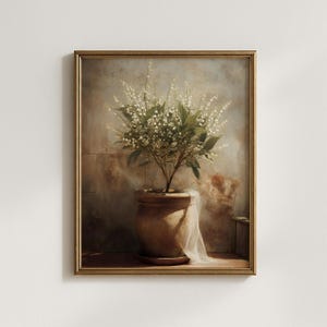 May include: A framed botanical print showing a small tree with white flowers and green leaves in a terracotta pot. A sheer white fabric drapes from the pot. The artwork is set against a neutral, textured background.
