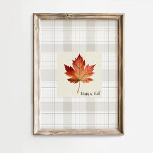 Pode incluir: Uma impressão emoldurada com uma folha de bordo em aquarela em tons de vermelho e laranja, com a inscrição "Happy Fall". O fundo tem um padrão xadrez cinza e branco, e a moldura é de madeira. Decoração de outono.