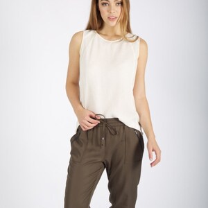 May include: A woman wearing a white sleeveless top and olive green drawstring pants with side pockets.