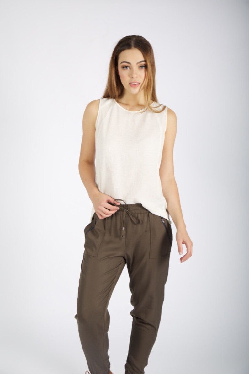 May include: A woman wearing a white sleeveless top and olive green drawstring pants with side pockets.