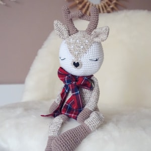May include: A crocheted deer toy with closed eyes, brown and white fur, and a red and black plaid scarf.