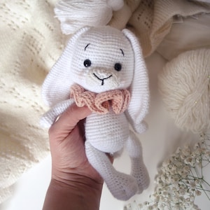 Peut inclure: Un lapin en crochet blanc avec un nœud rose. Le lapin a des yeux noirs et un sourire cousu.