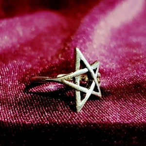 May include: A silver pentagram ring on a deep red velvet background.