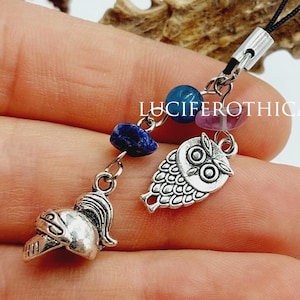 May include: A silver-toned charm with an owl pendant, a knight's helmet, and colorful beads. The charm is attached to a black cord. The text "LUCIFEROTHICA" is visible.