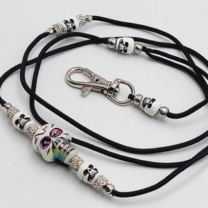 Puede incluir: Lanyard negro con un dije de calavera blanca y detalles de strass. El lanyard tiene un clip plateado y mide aproximadamente 76 cm de largo.