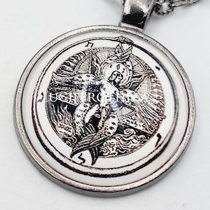 May include: A round silver-toned pendant necklace featuring a black and white circular graphic of a winged figure within a geometric seal. The pendant is attached to a matching silver-toned metal chain link necklace with a smooth, polished finish.